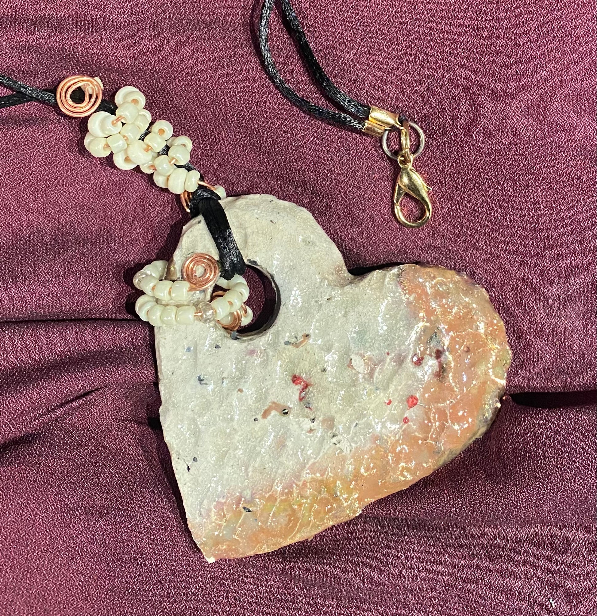 Have A Heart ! Each heart pendant is handmade with love! It is 3" x 3" and weighs approx. 3ozs. It has white metallic raku glazes that renders a unique translucent  patina. The heart is textured and holds a  spiral of white pony beads on copper wire.  This pendant has a nice 12"black rattail cord!